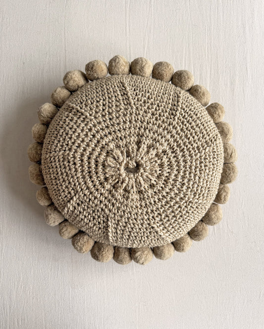 Back view of a Beige-Sand colored round cushion with handmade pom poms.