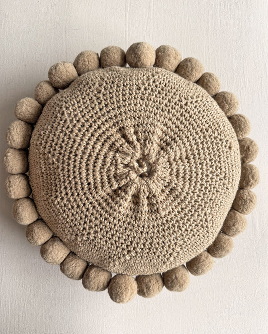 Back view of a Beige-Sand colored round cushion with handmade pom poms.
