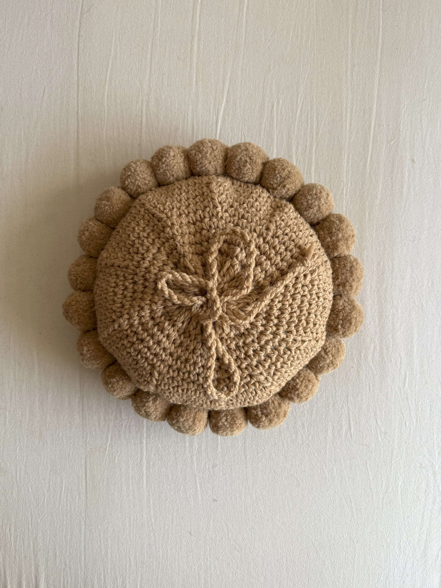 Back view of a b¿Beige-Sand colored round cushion with handmade pom poms.