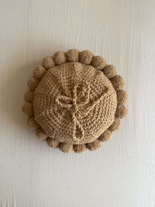 Back view of a b¿Beige-Sand colored round cushion with handmade pom poms.