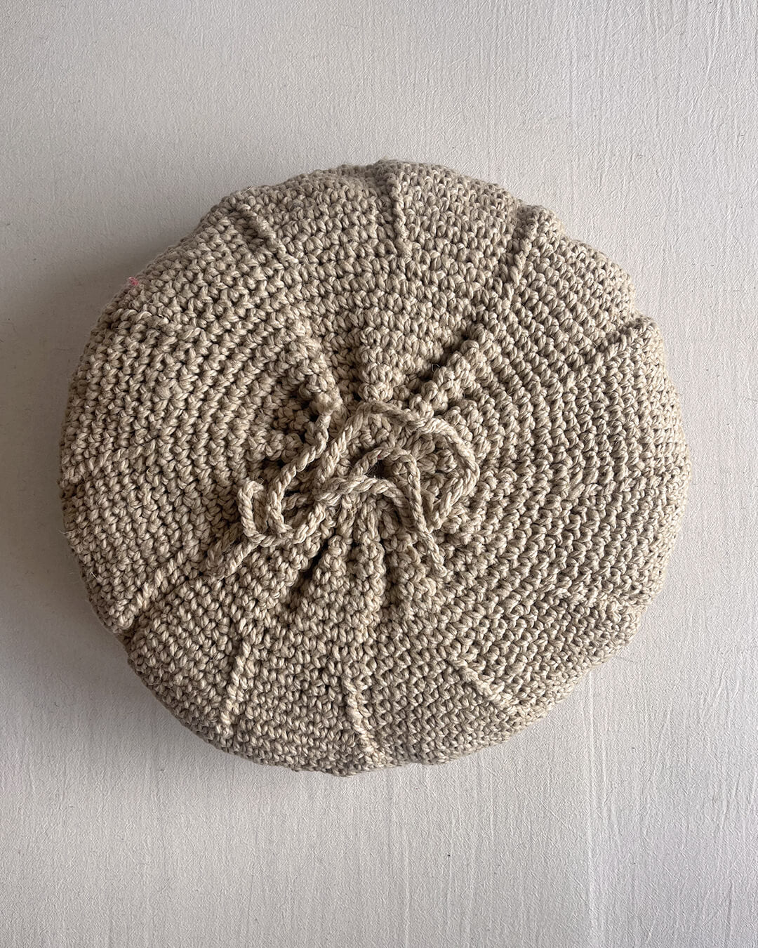 Back of a Beige-Sand round cushion made of handwoven wool, with visible woolen tie closure.