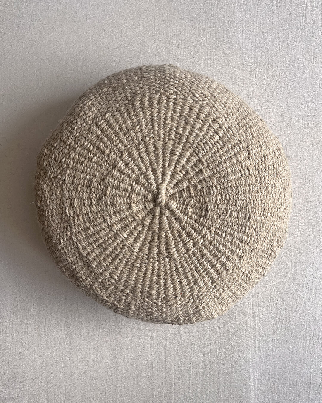 Beige-Sand colored round cushion made of handwoven wool, shown from the front.