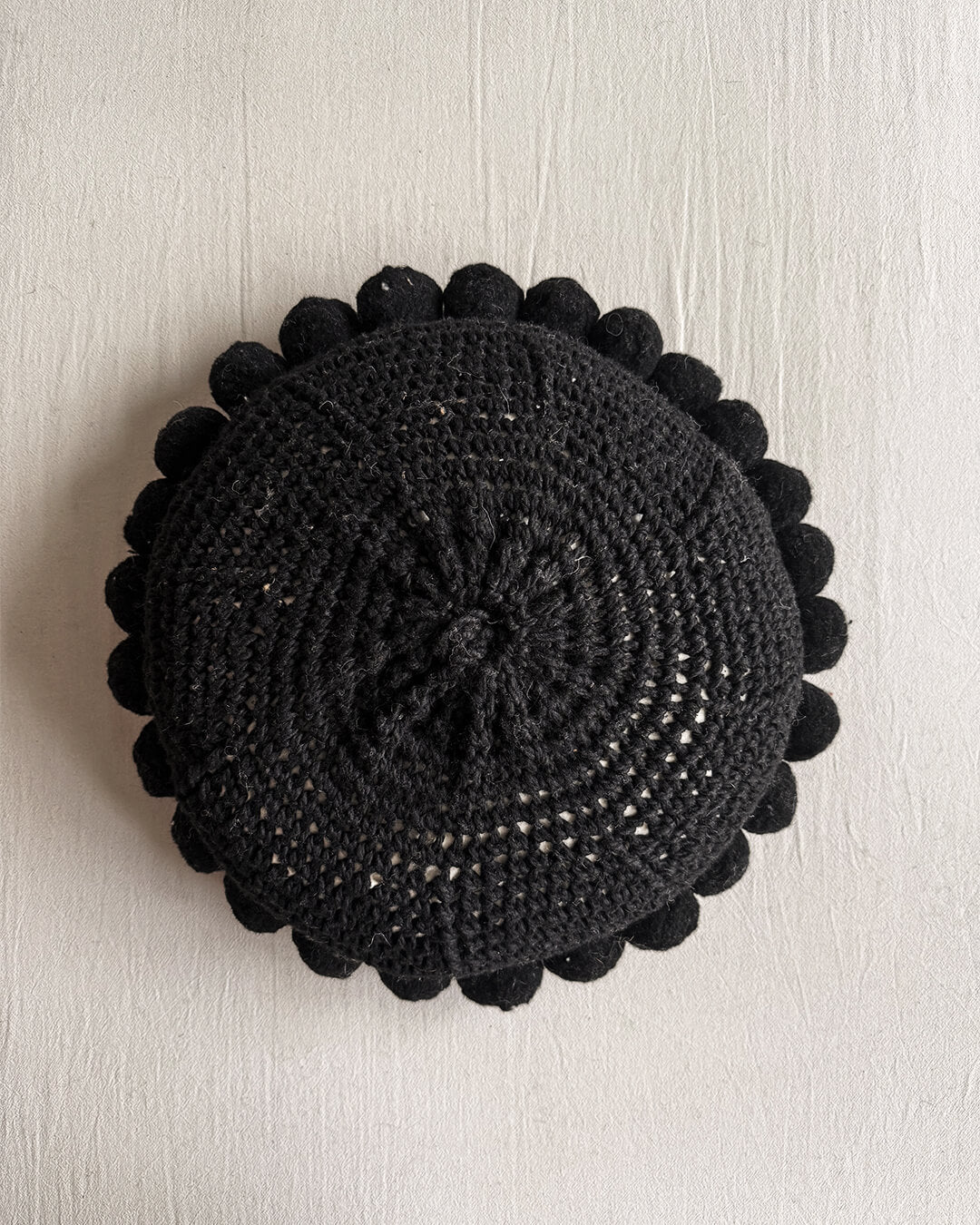 Black-colored round cushion with handmade pom poms, shown from the back.