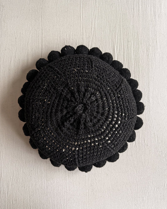Black-colored round cushion with handmade pom poms, shown from the back.