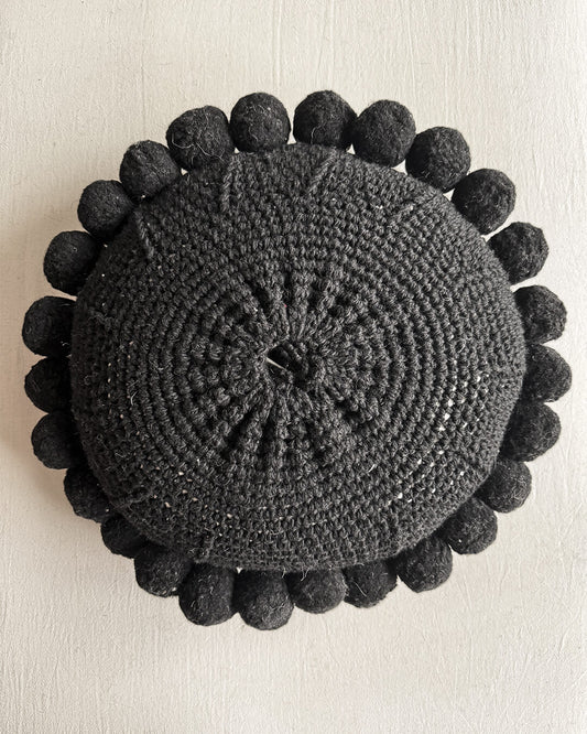 Black-colored round cushion with handmade pom poms, shown from the back.
