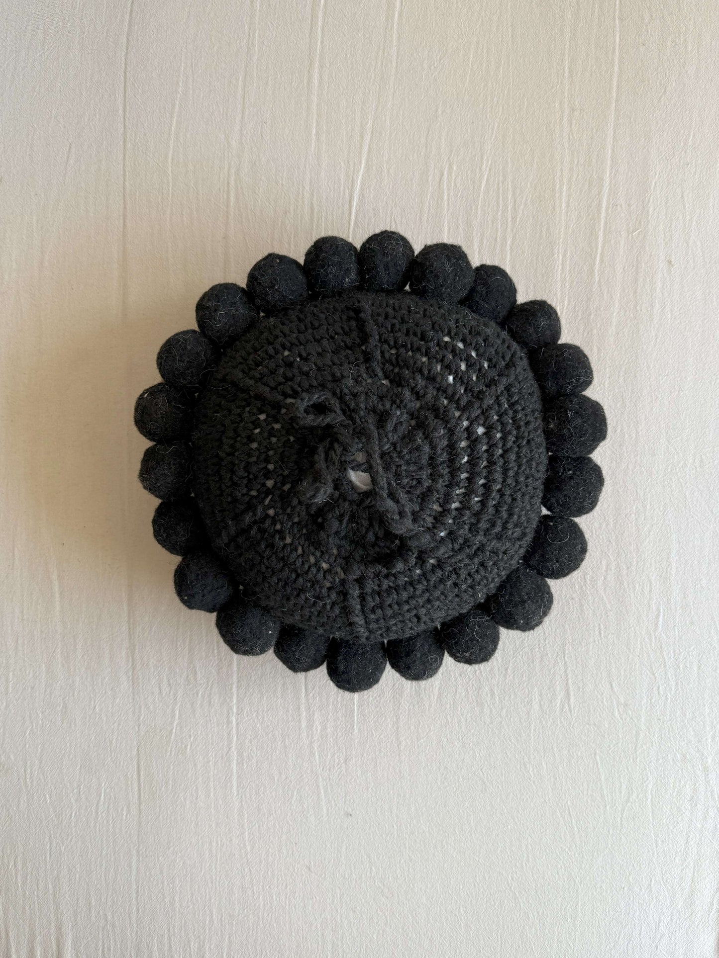 Black-colored round cushion with handmade pom poms, shown from the back.