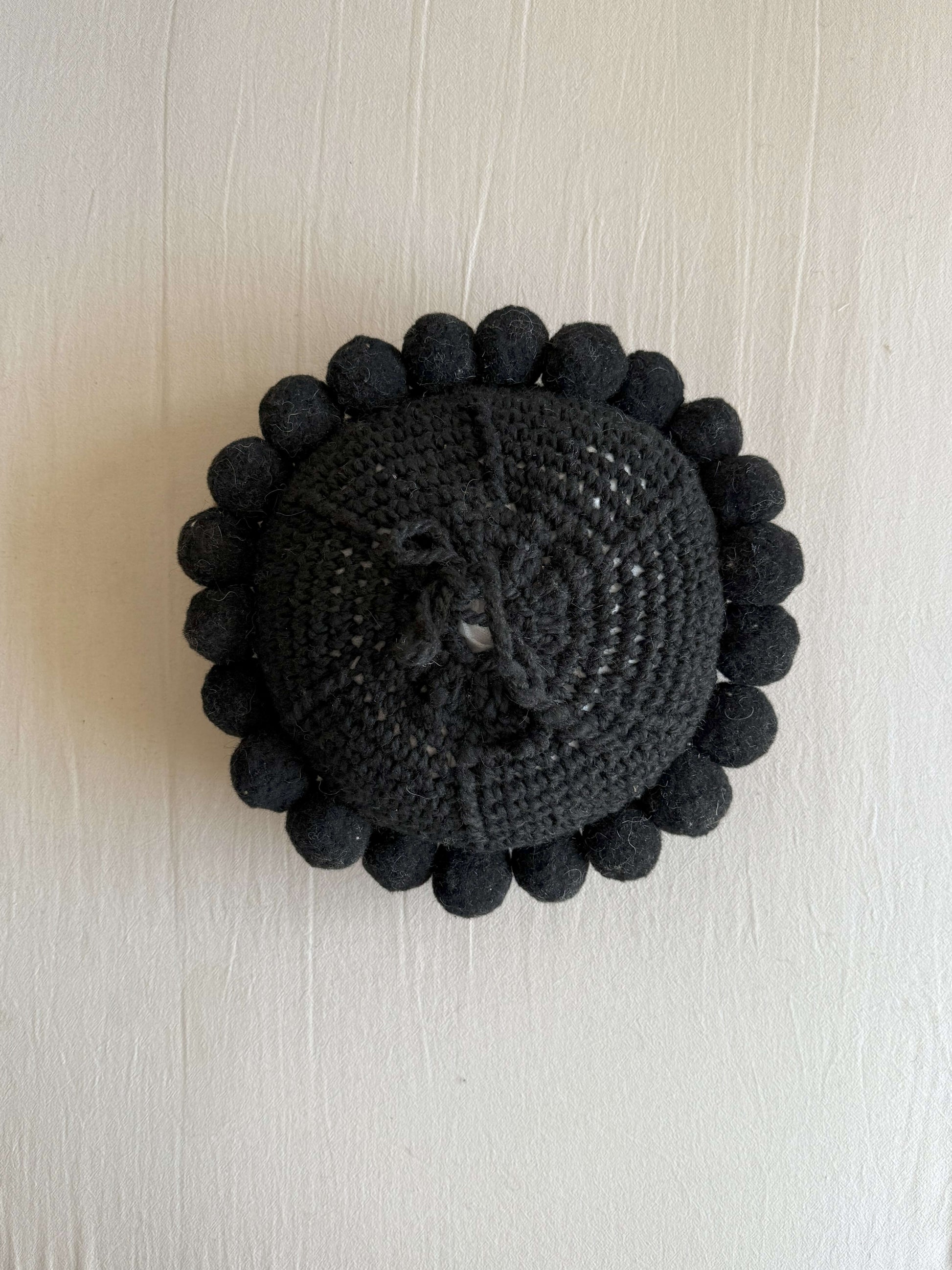 Black-colored round cushion with handmade pom poms, shown from the back.