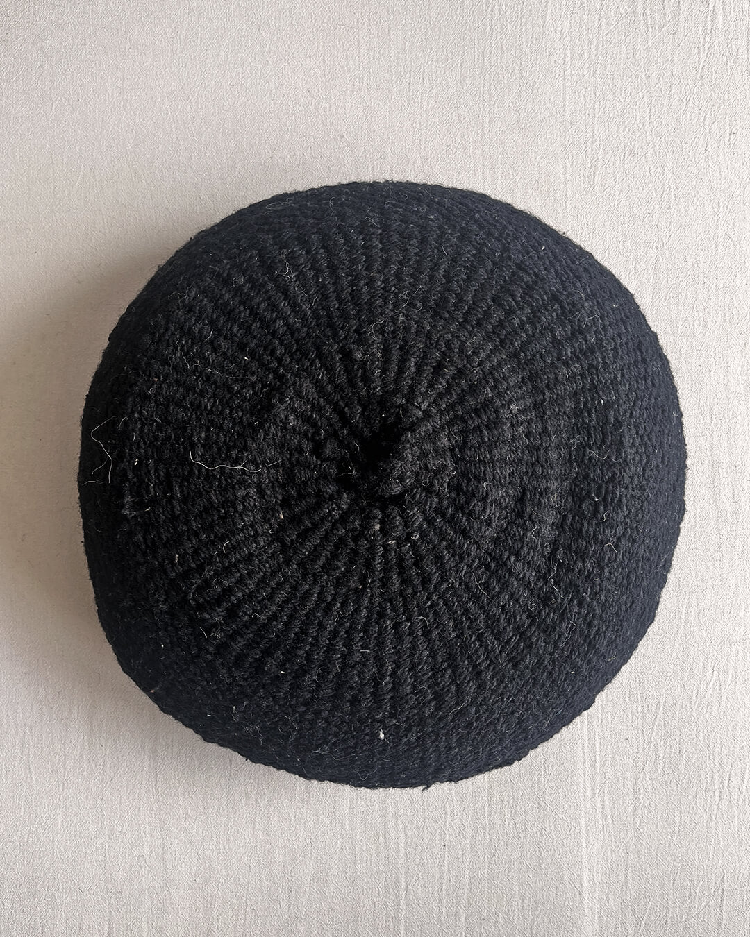 Black-colored round cushion made of handwoven wool, shown from the front.