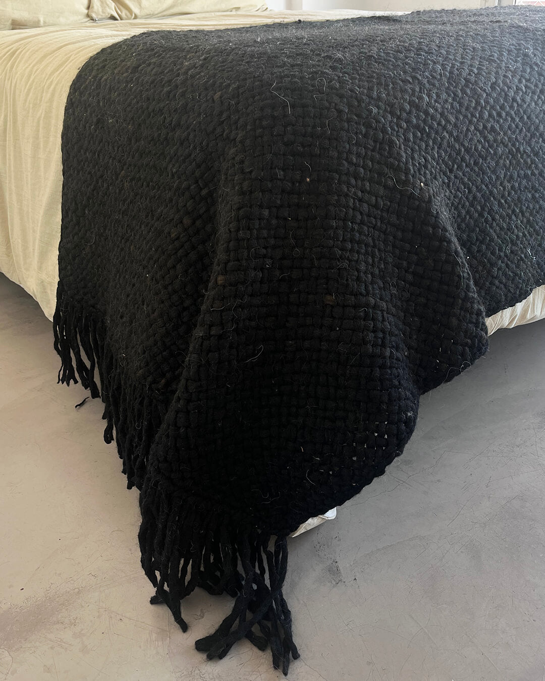 Full Black wool throw covering a bed, showing its size and weight.
