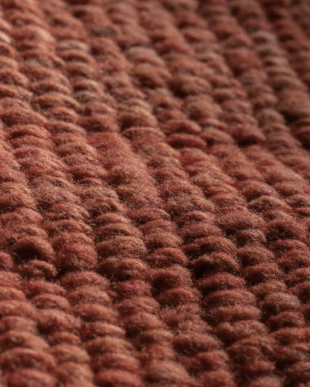 Close-up of a handwoven wool rug in burgundy tone showing a thick, looped texture and natural fiber variation.