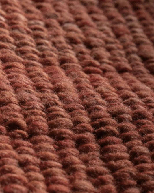 Close-up of a handwoven wool rug in burgundy tone showing a thick, looped texture and natural fiber variation.