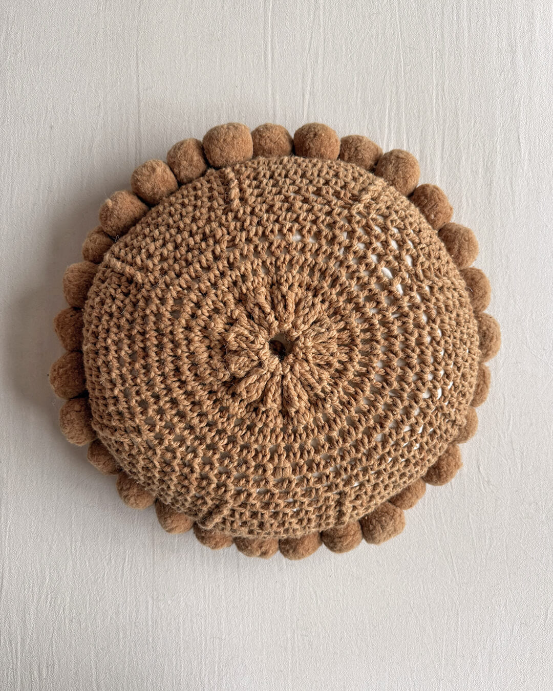 Back of a Camel-colored round wool cushion with visible woolen cords.