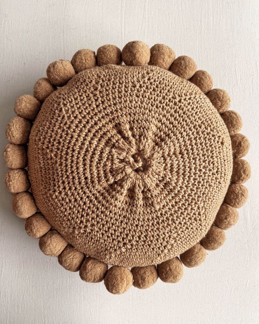 Back of a camel-colored round wool cushion with visible woolen cords.