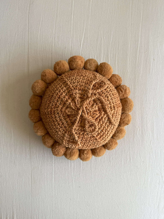 Back of a Camel-colored round wool cushion with visible woolen cords.