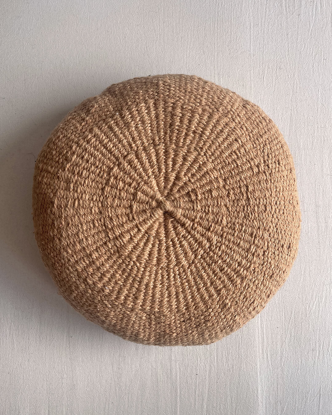 Camel-colored round cushion made of handwoven wool, shown from the front.