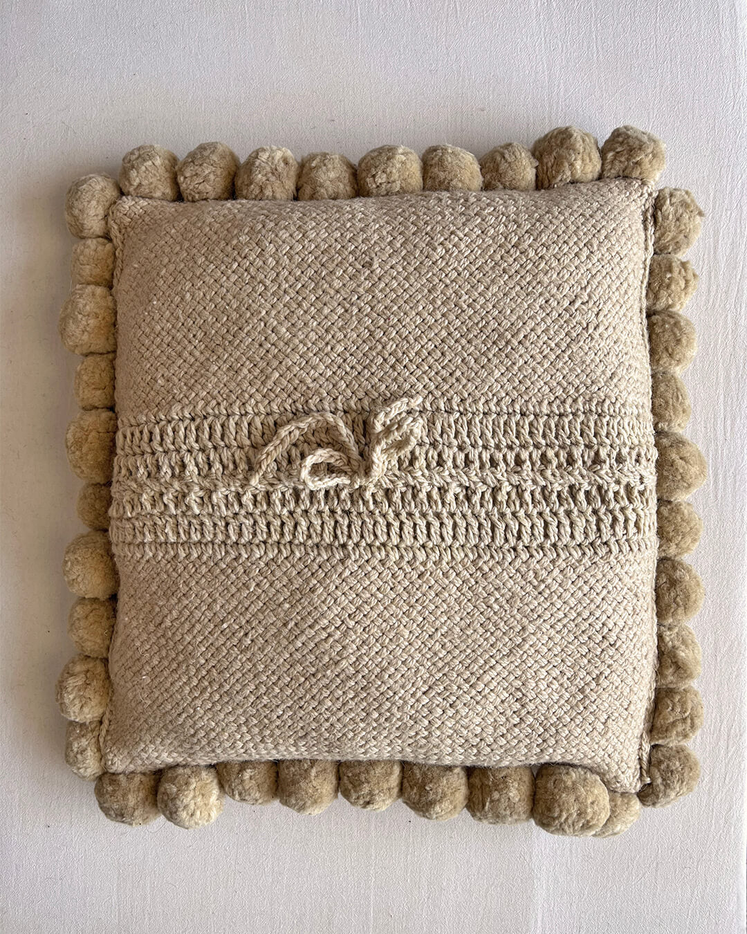 Beige-Sand colored square cushion with handmade pom poms, shown from the back.