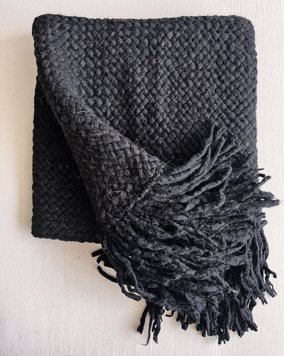 Black wool throw partially unfolded, displaying its thick texture and twisted fringes.