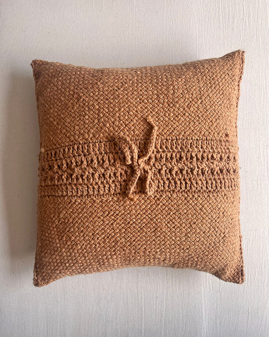 Camel-colored square wool cushion, shown from the back with woolen tie closure.