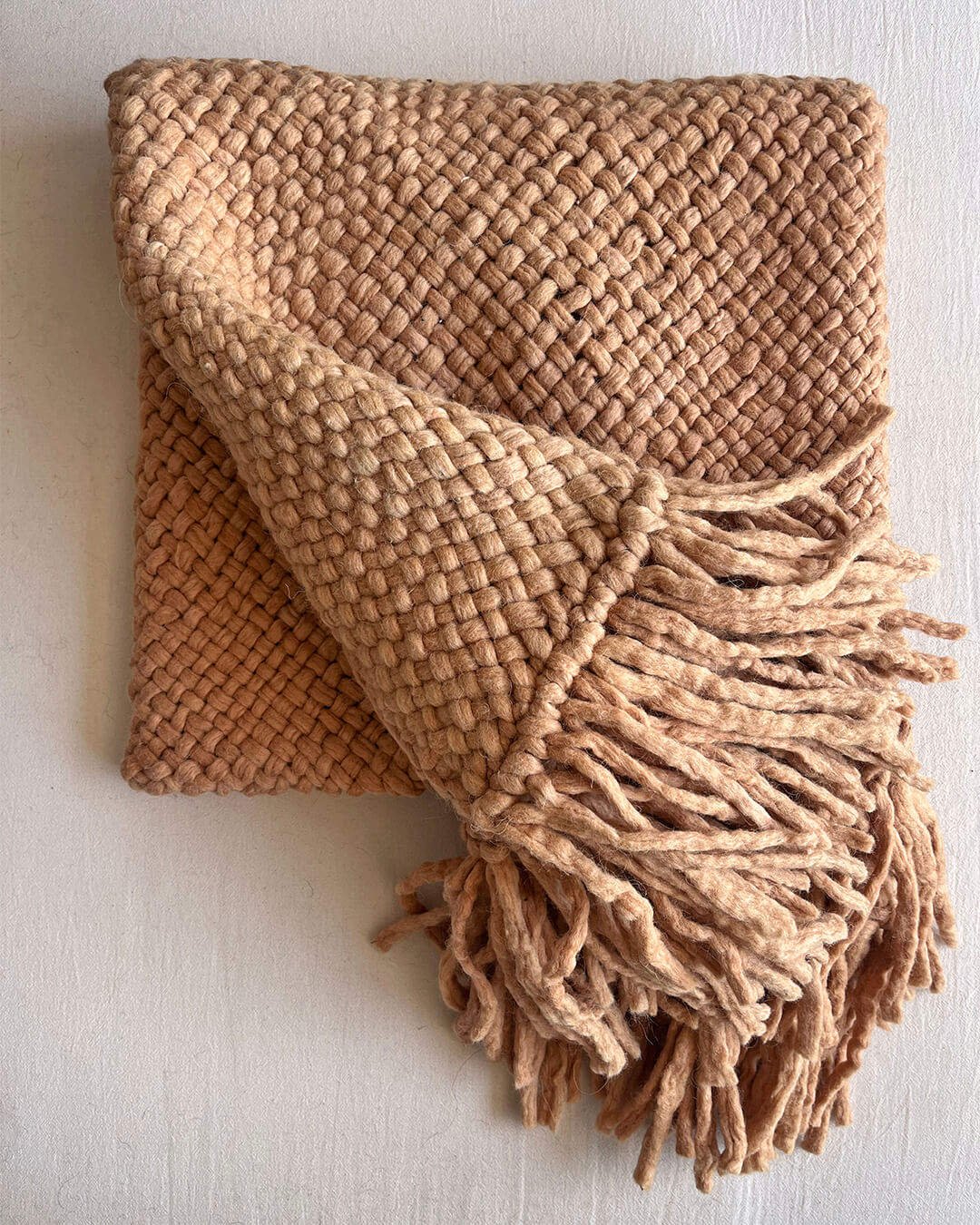 Camel wool throw partially unfolded with visible fringes and woven pattern.
