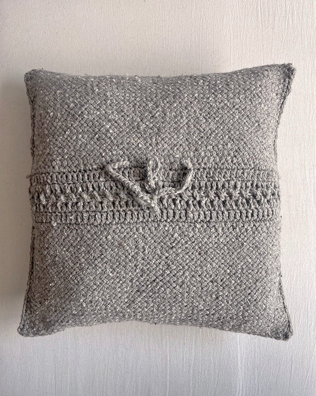 Gray-colored square wool cushion, shown from the back with woolen tie closure.