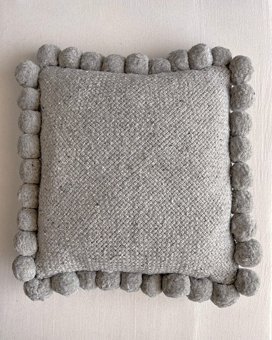 Gray-colored square cushion with handmade pom poms, shown from the front.