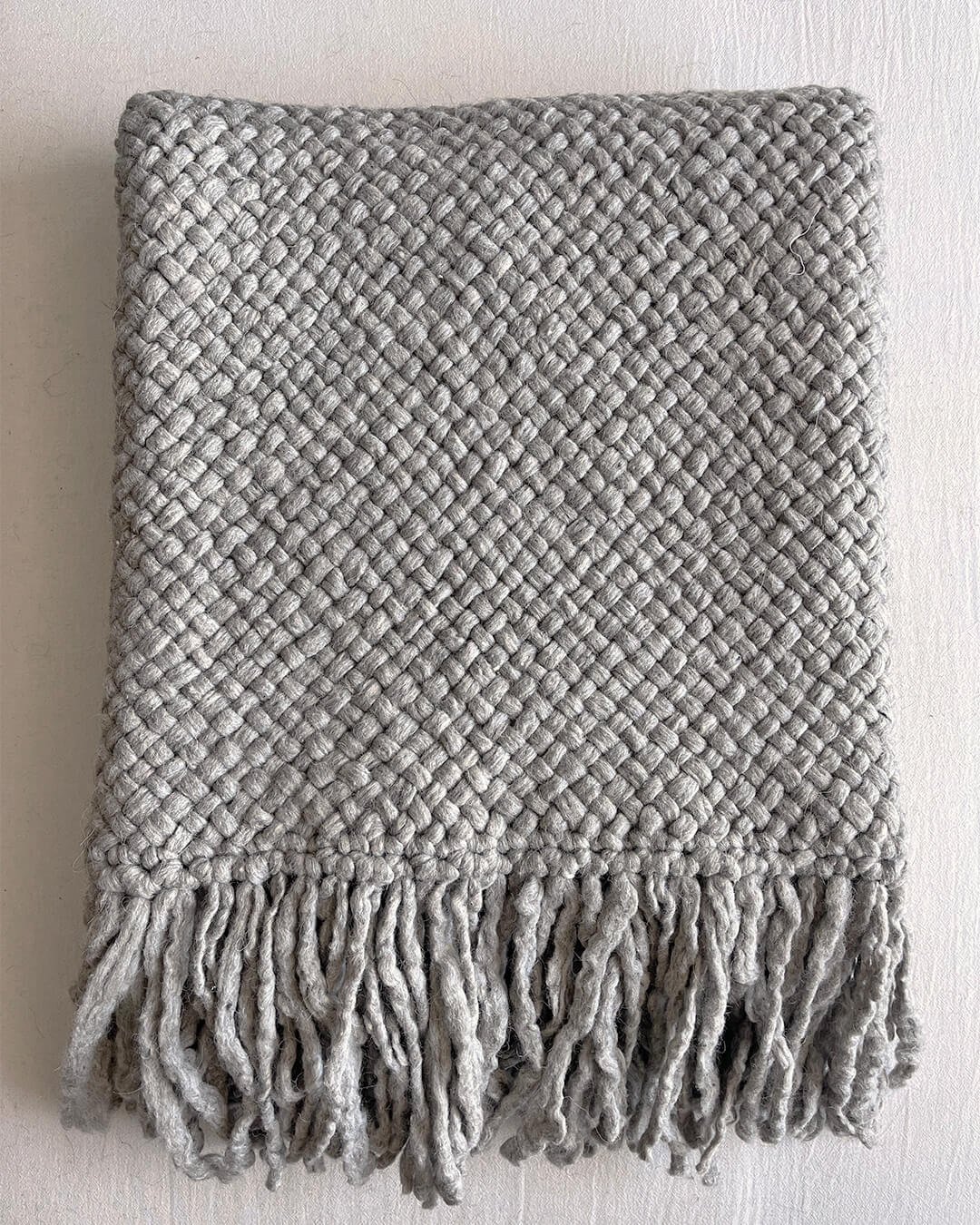 Folded Gray wool throw with visible texture and fringe on white background.