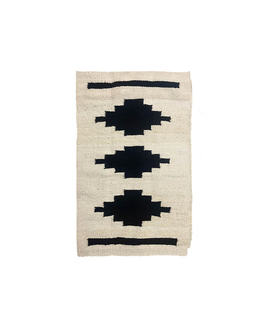 Handwoven CHACO Mini Rug with three black geometric shapes on a natural wool background.