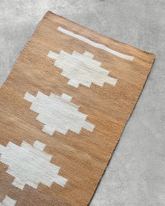 Close-up of the CHACO Mini Rug in natural brown tones, handwoven with white geometric patterns on llama wool.