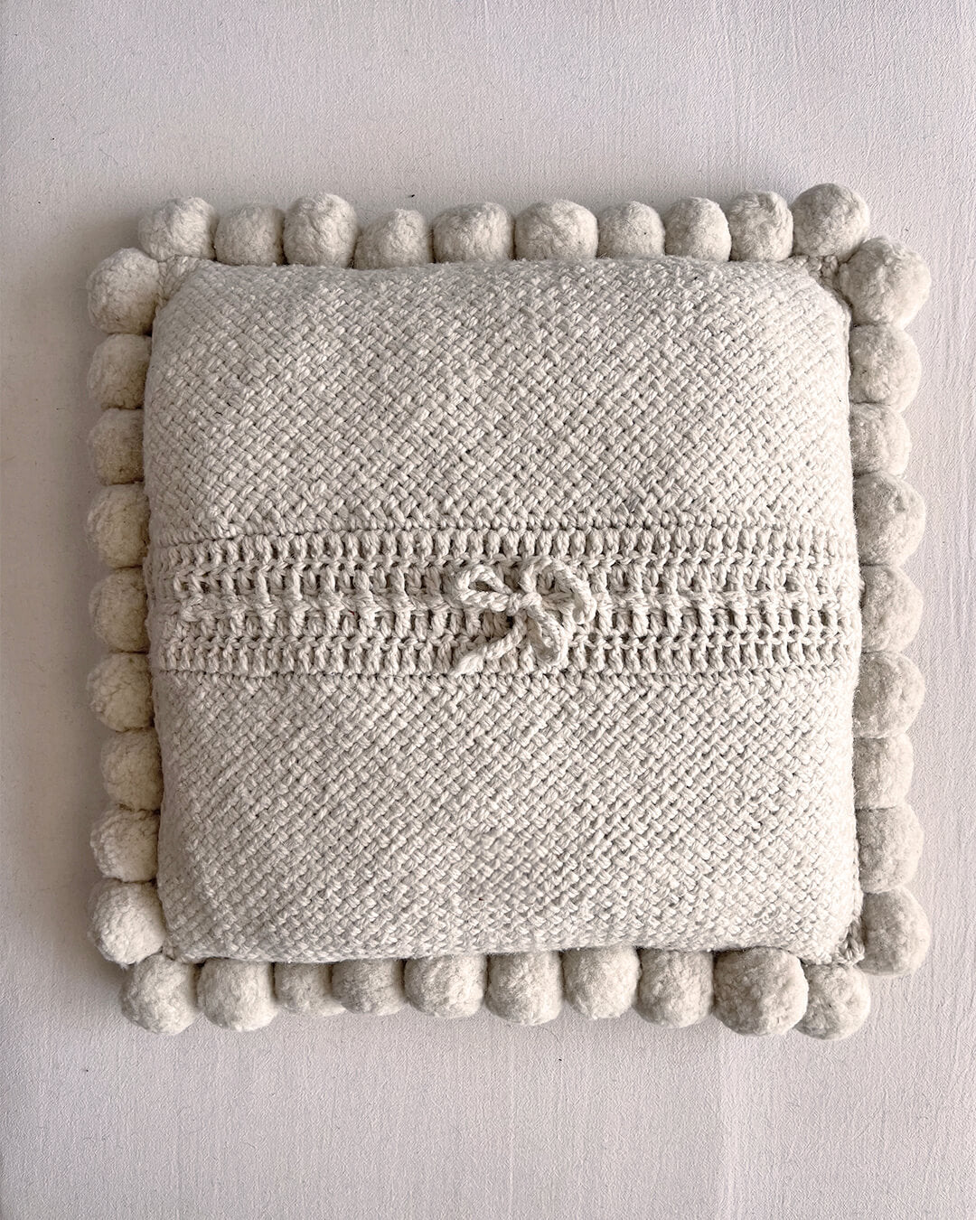Natural White square cushion with handmade pom poms, shown from the back.
