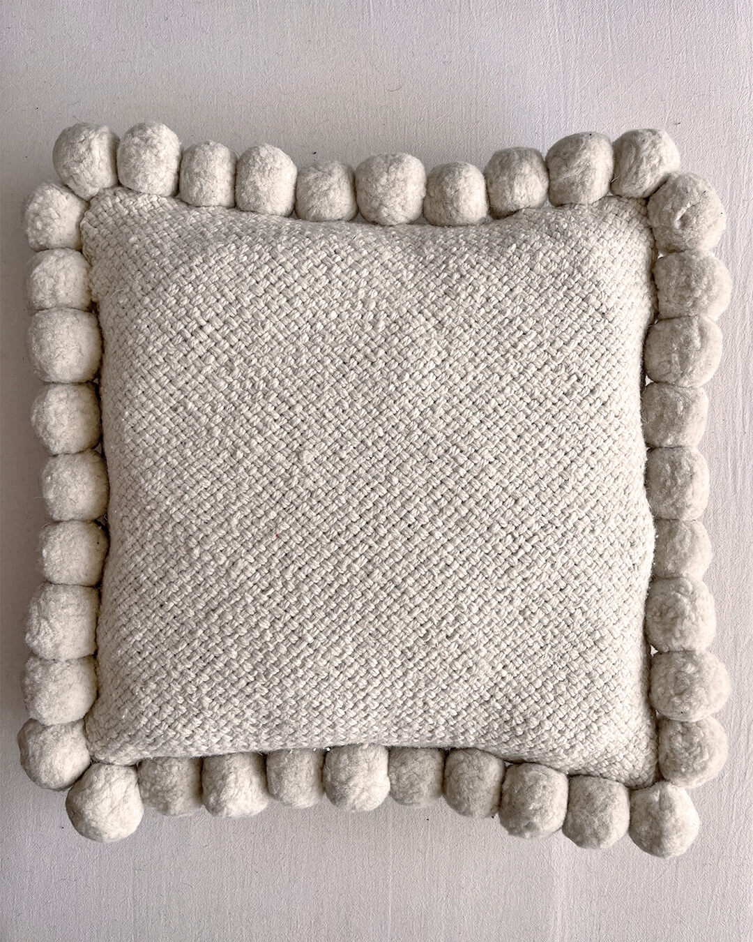 Natural White square cushion with handmade pom poms, shown from the front.
