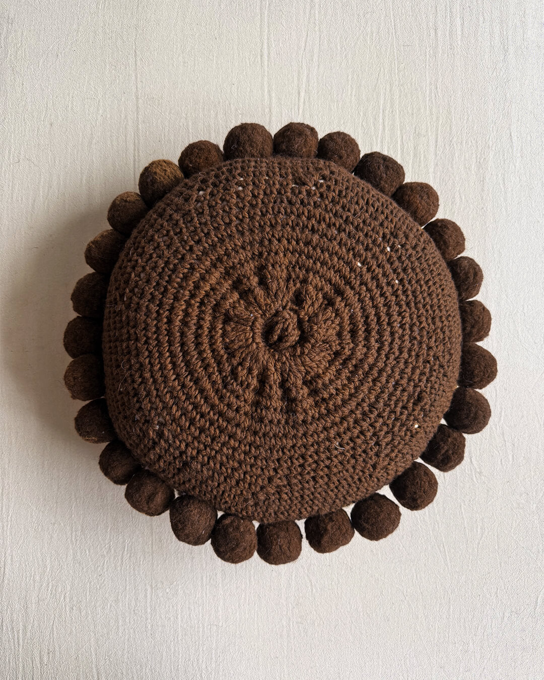 Chocolate Brown-colored round cushion with handmade pom poms, shown from the back.