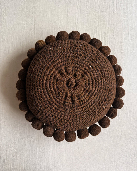 Chocolate Brown-colored round cushion with handmade pom poms, shown from the back.
