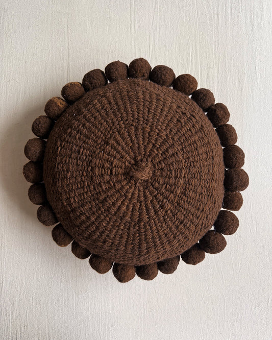 Chocolate Brown-colored round cushion with handmade pom poms, shown from the front.