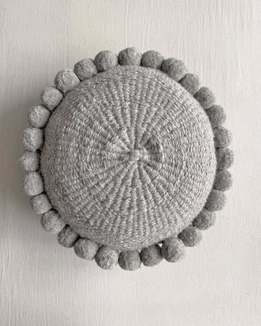Gray-colored round cushion with handmade pom poms, shown from the front.