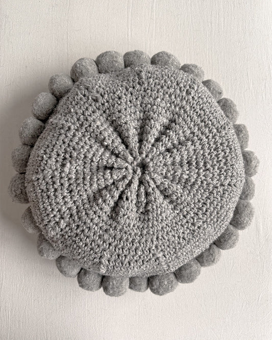 Gray-colored round cushion with handmade pom poms, shown from the back.