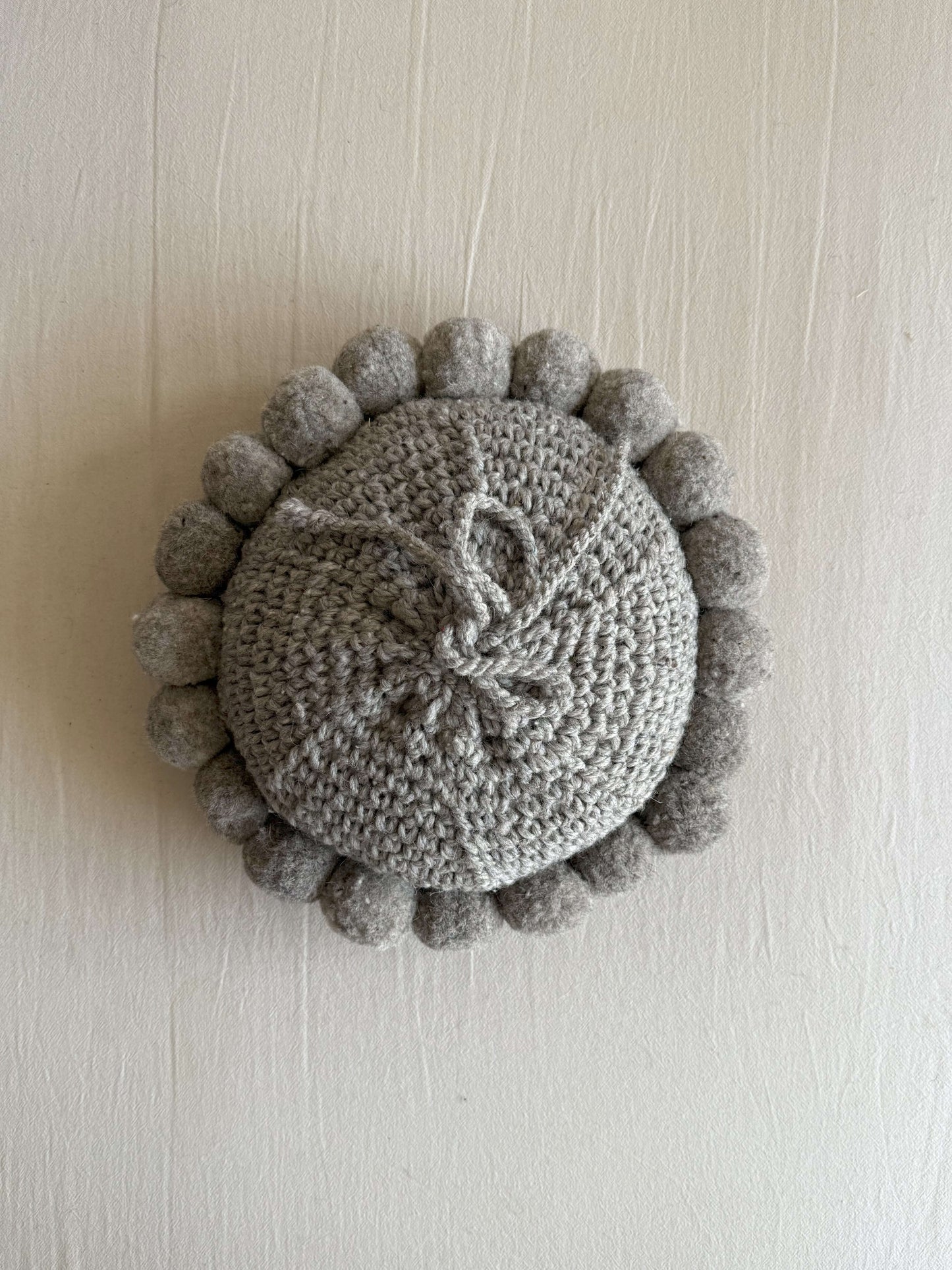 Gray-colored round cushion with handmade pom poms, shown from the back.