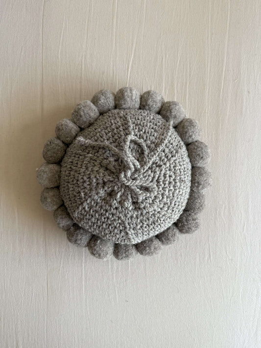 Gray-colored round cushion with handmade pom poms, shown from the back.