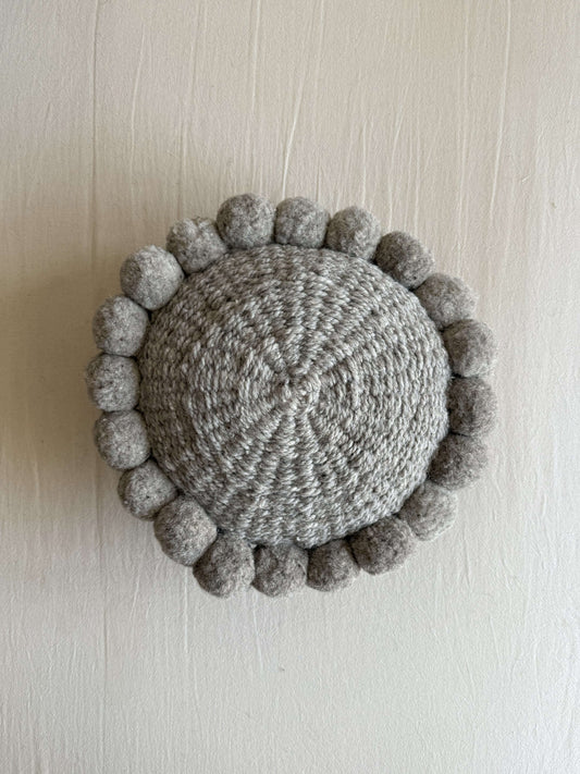 Gray-colored round cushion with handmade pom poms, shown from the front.