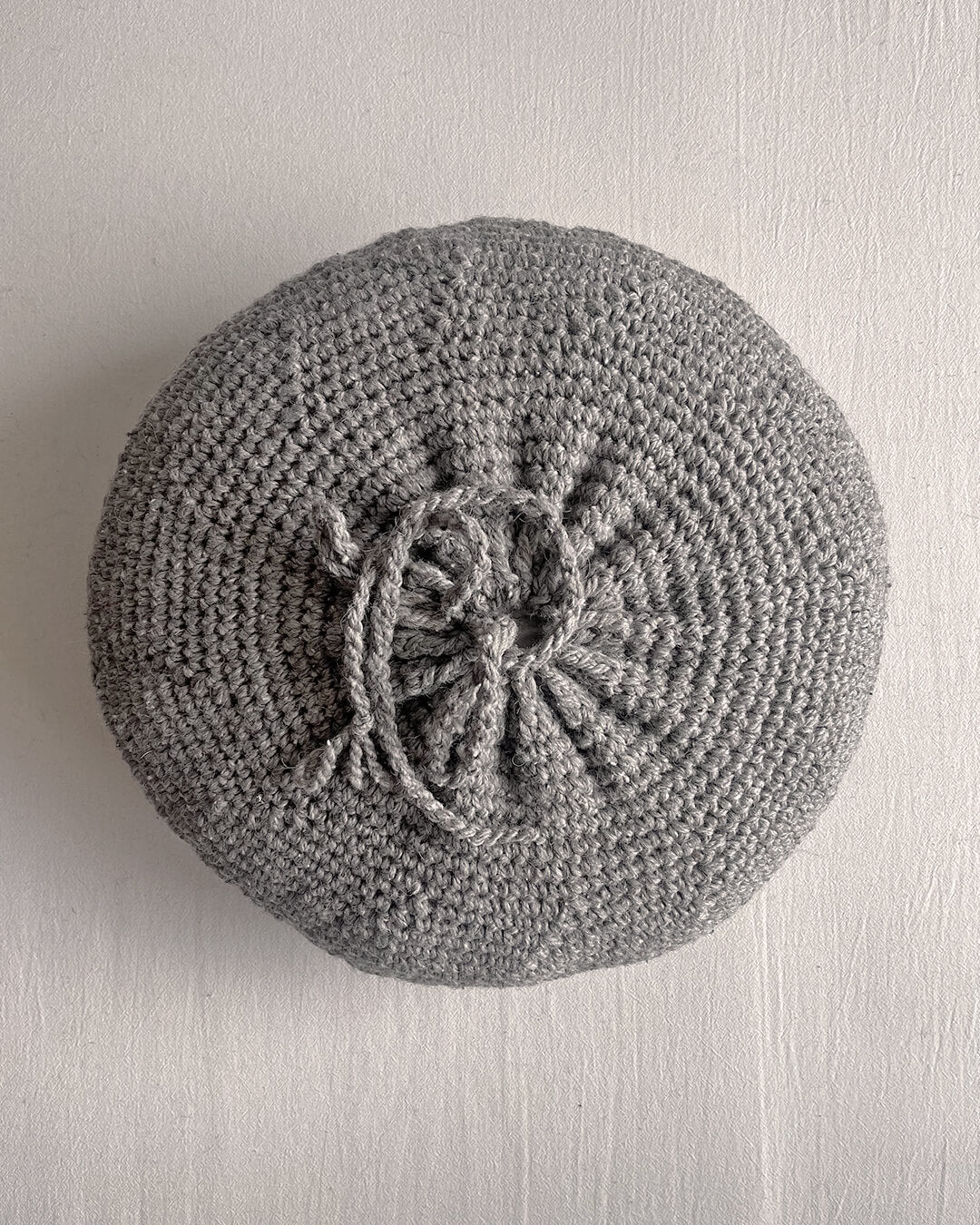 Back of a Gray round cushion made of handwoven wool, with visible woolen tie closure.