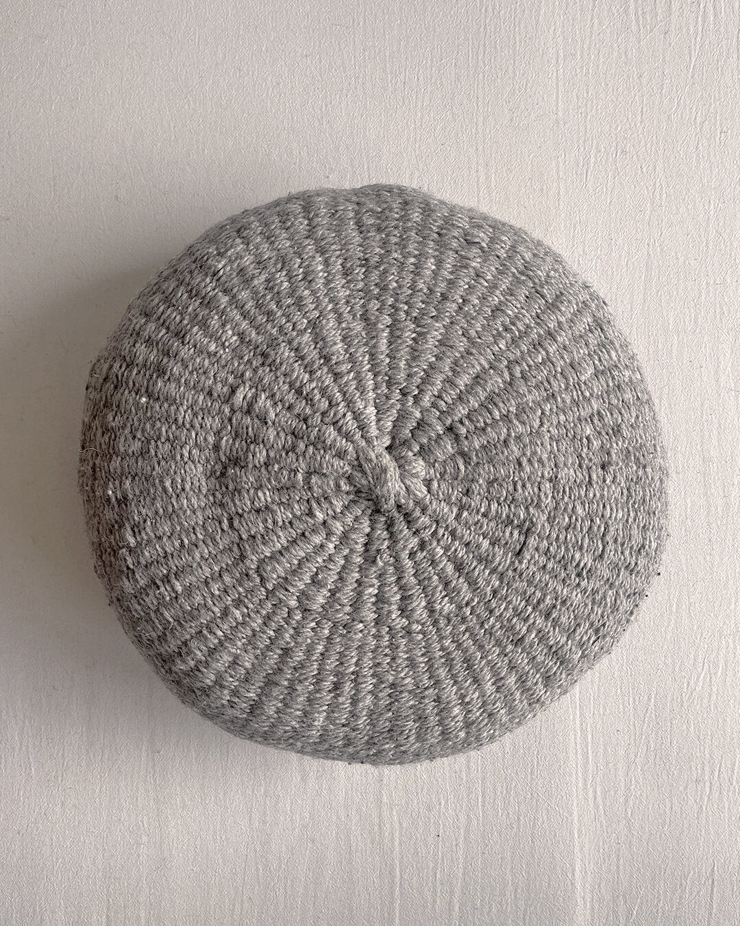 Gray-colored round cushion made of handwoven wool, shown from the front.