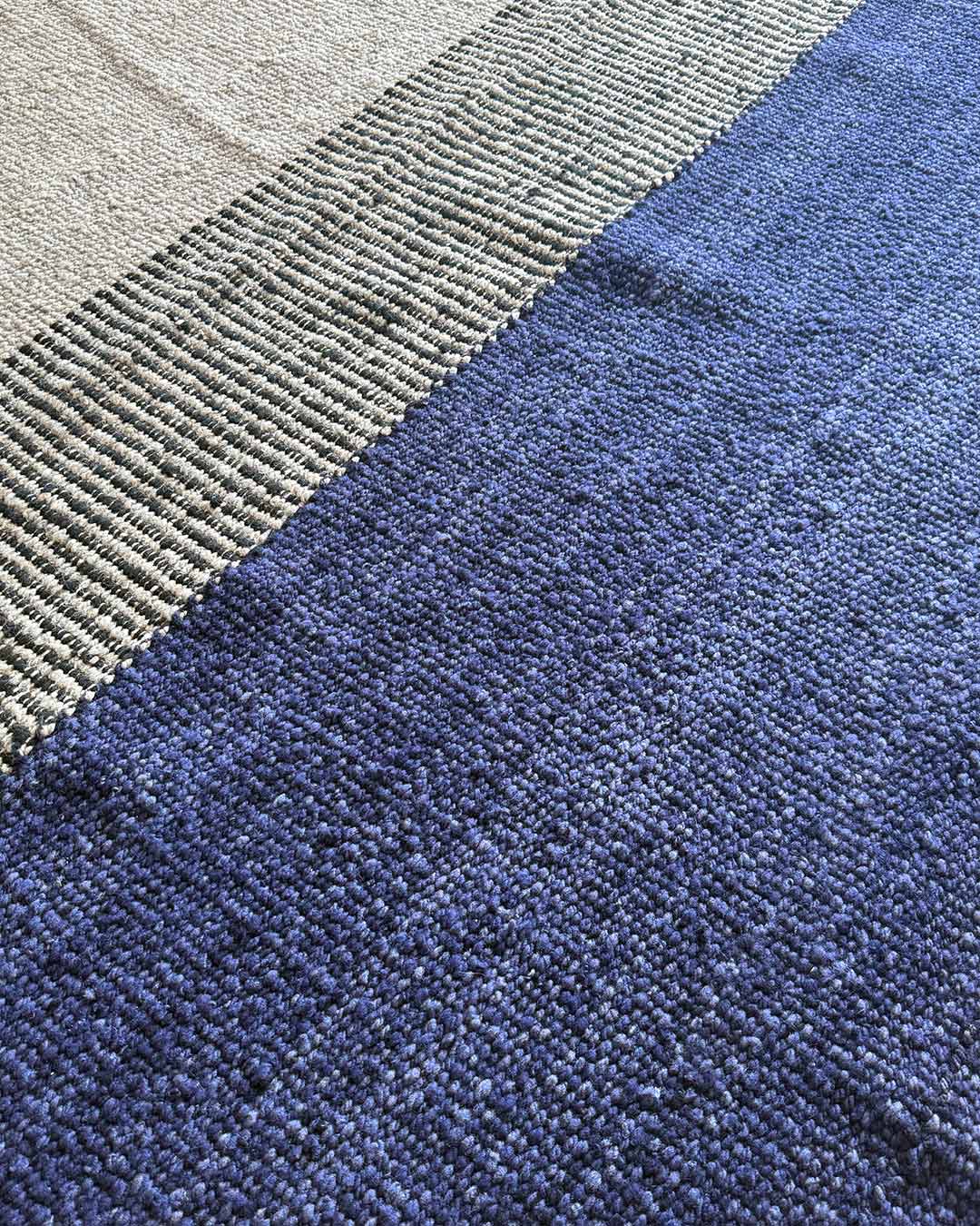 Close-up of a handwoven rug emphasizing the contrast between a deep midnight blue field and a black-and-natural woven section.