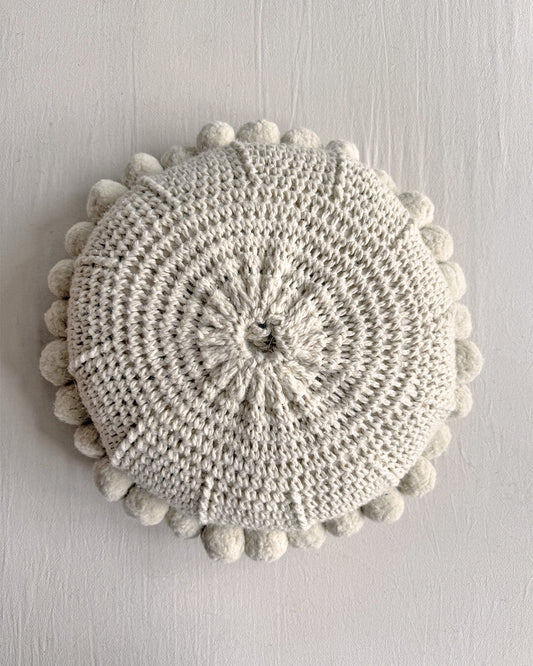 Natural White-colored round cushion with handmade pom poms, shown from the back.