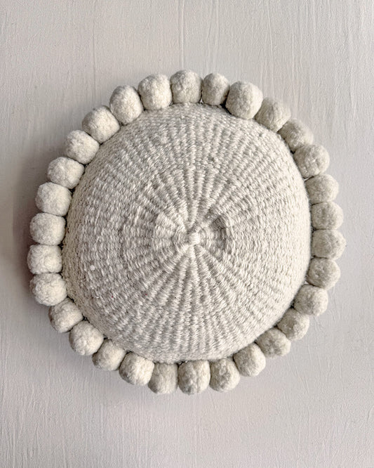 Natural White-colored round cushion with handmade pom poms, shown from the front.