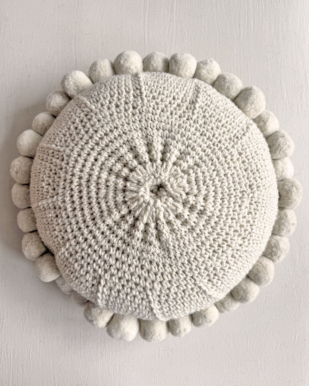 Natural White-colored round cushion with handmade pom poms, shown from the back.