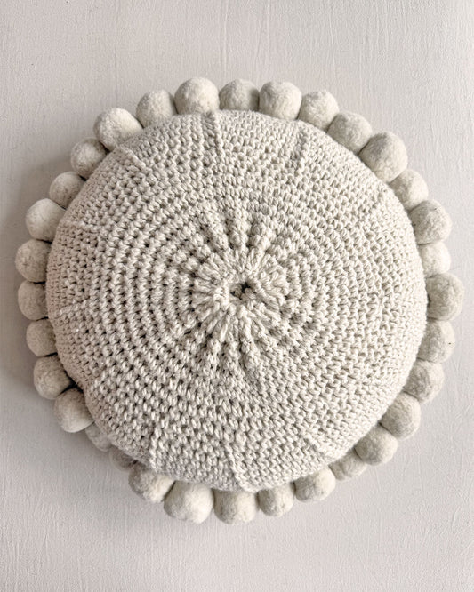 Natural White-colored round cushion with handmade pom poms, shown from the back.