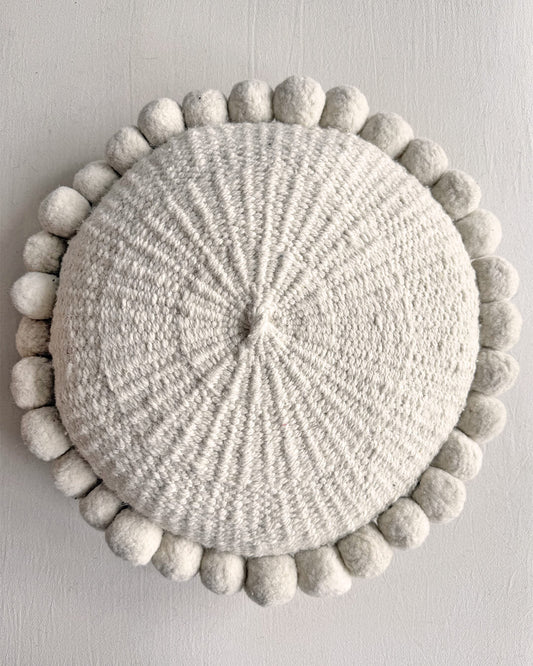 Natural White-colored round cushion with handmade pom poms, shown from the front.