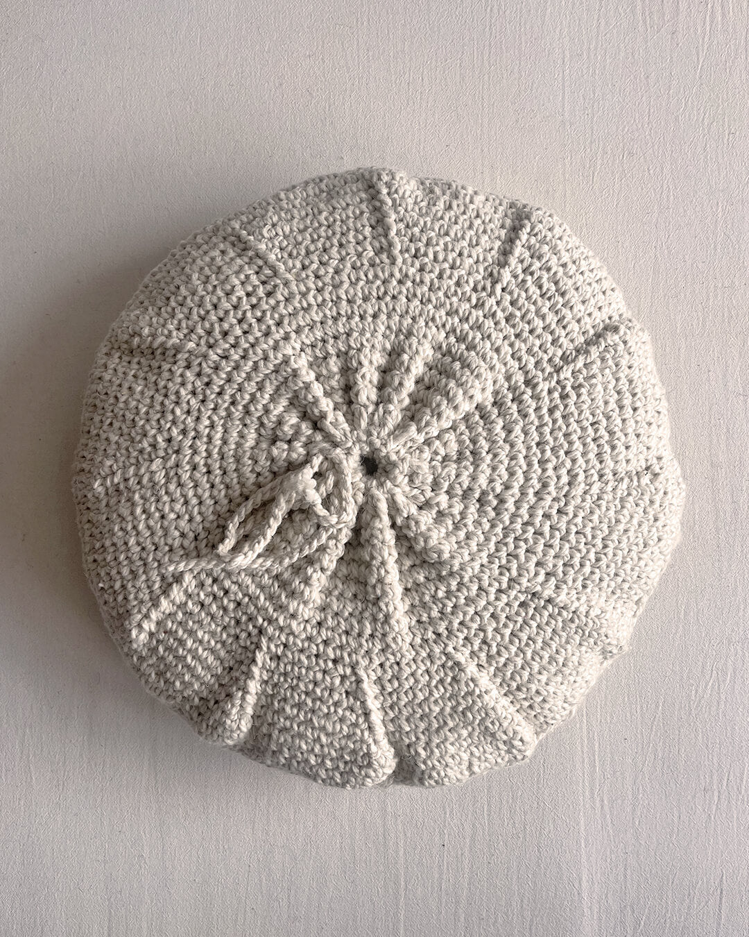Back of a Natural White round cushion made of undyed handwoven wool, with visible woolen tie closure.
