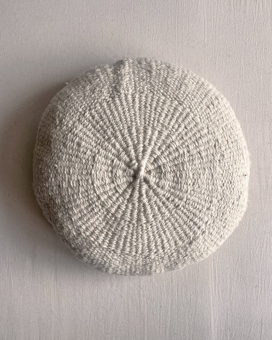 Natural White round cushion made of undyed handwoven wool, shown from the front.