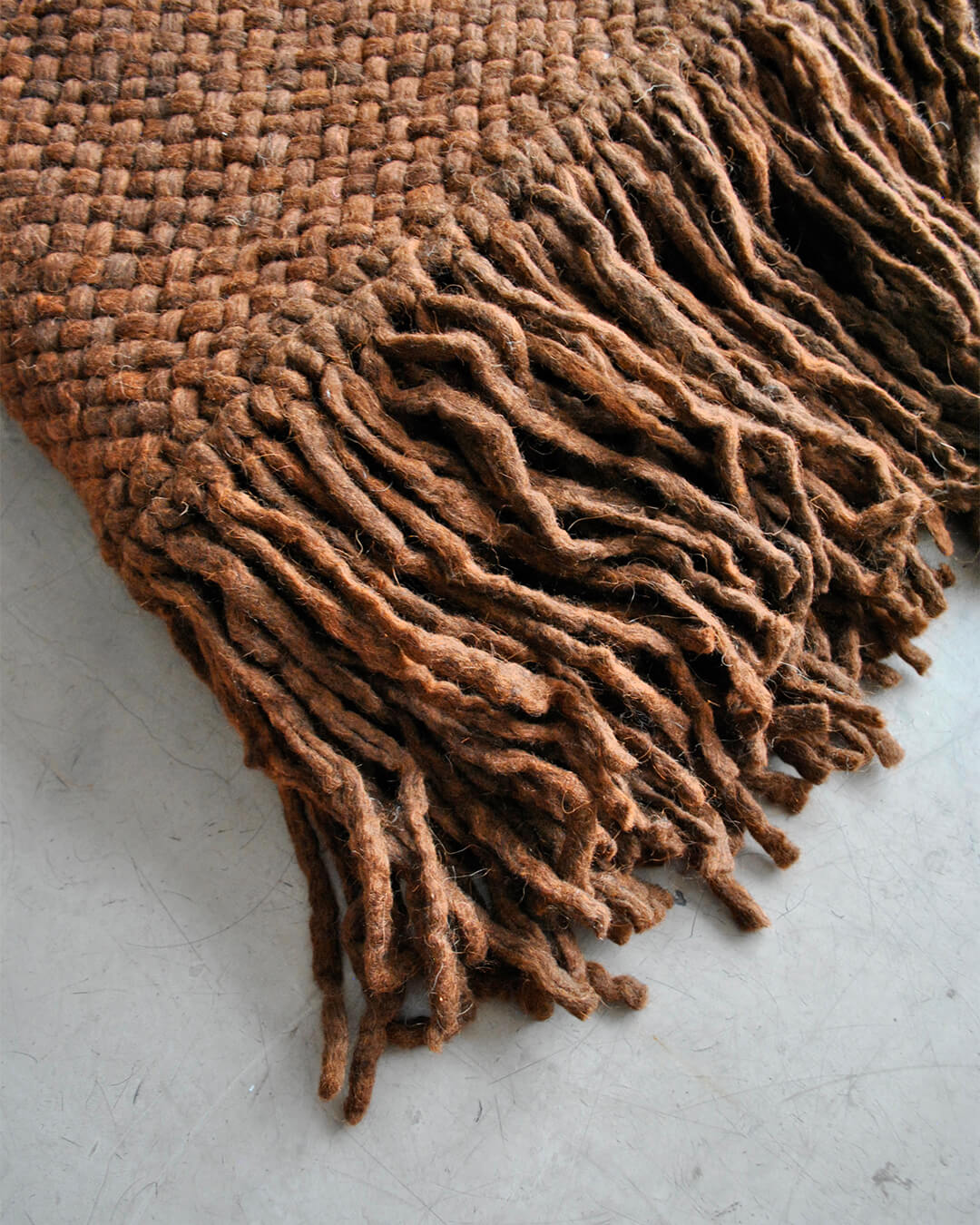 Chocolate Brown wool throw fringe detail resting on a smooth floor.
