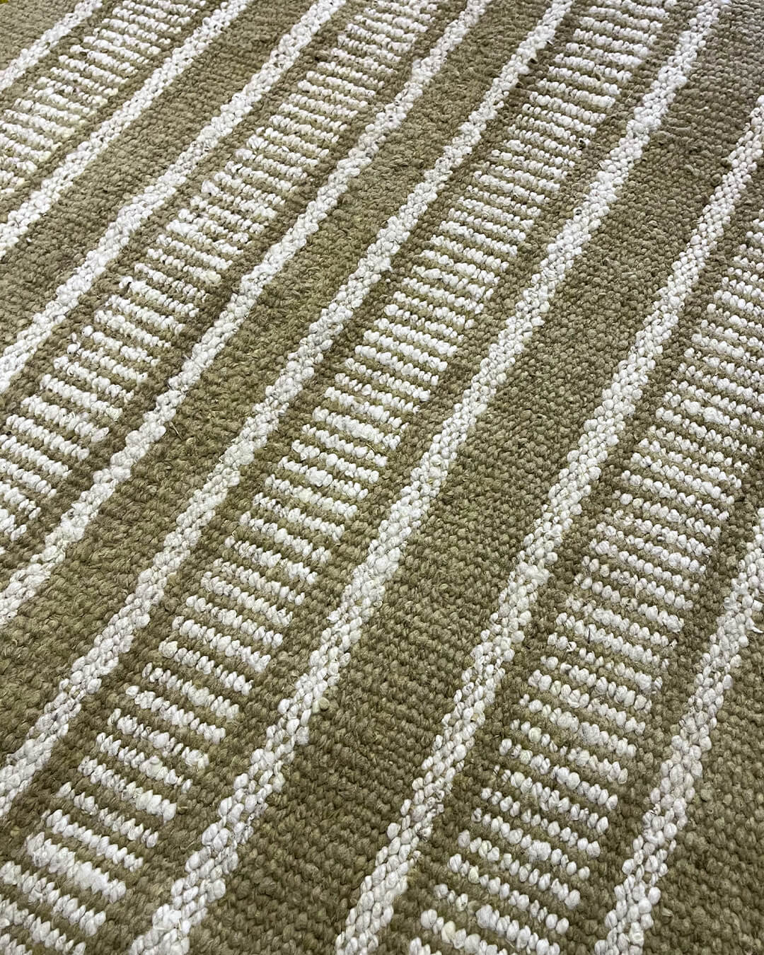 Close-up of a handwoven wool rug with comb-striped pattern in yerba green and natural wool tones.